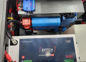 Close-up of an electrical setup featuring an EPOCH 12.8V 460Ah battery, a Victron inverter, switches, wiring, and various connected electronic components arranged in an organized manner.