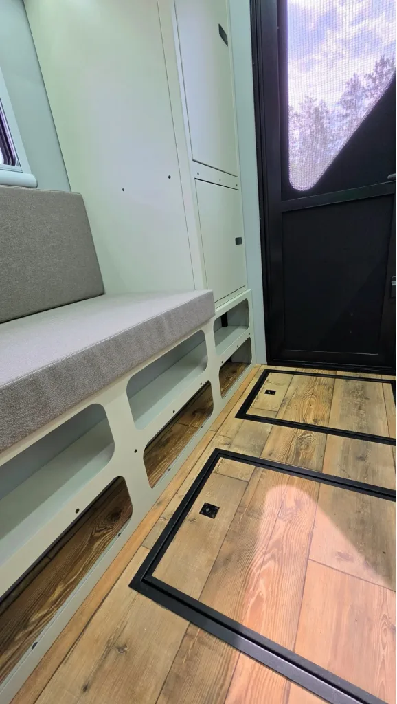 Interior of a light-green seating area with a gray bench, storage cabinets, and wood-look flooring beside a mesh-front door.